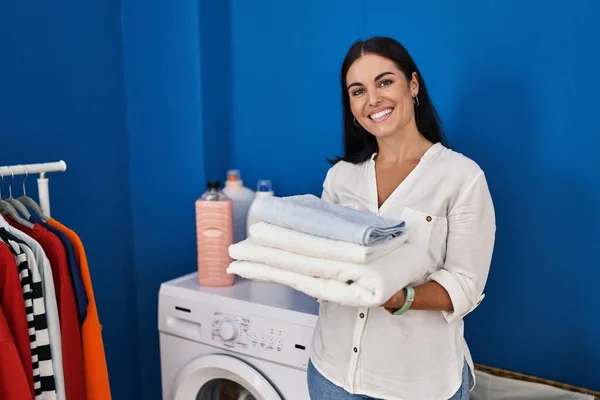 年轻美丽的惊慌失措的女人微笑着 自信地拿着折叠的毛巾在洗衣房里 — 图库照片