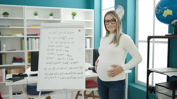 Young pregnant woman teacher teaching maths lesson touching belly at classroom
