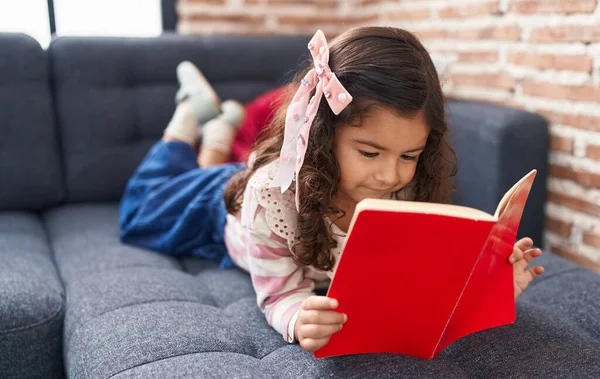 Adorable Hispanic Girl Reading Book Lying Sofa Home — Foto de Stock