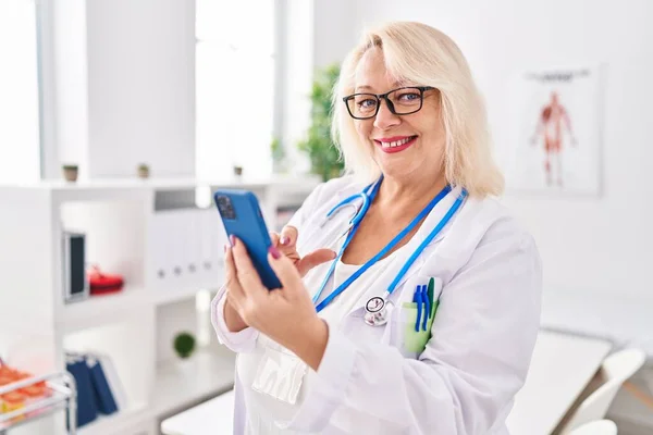 Μέση Ηλικία Ξανθιά Γυναίκα Φορώντας Στολή Γιατρού Χρησιμοποιώντας Smartphone Στην — Φωτογραφία Αρχείου