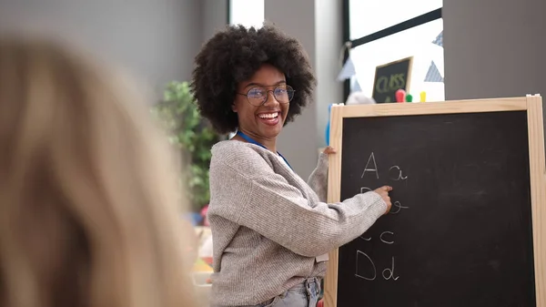アフリカ系アメリカ人の女性教師が幼稚園で黒板に自信を持って書く笑顔 — ストック写真