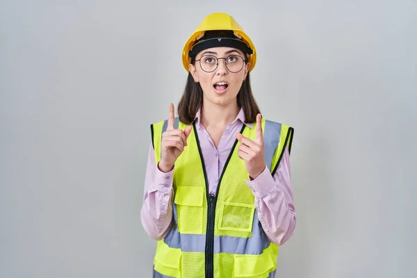 身穿建筑工人制服和硬礼帽的西班牙裔女孩惊奇地抬起头 用手指和胳膊指指着 — 图库照片