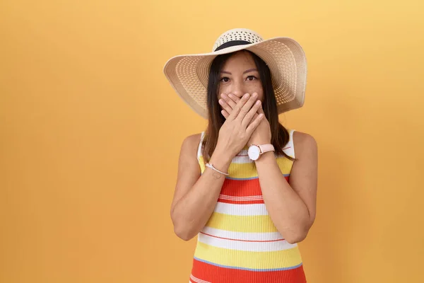 黄色の背景の上に夏の帽子を身に着けている中国の女性は間違いのための手で口を覆うショックを受けた 秘密の概念 — ストック写真
