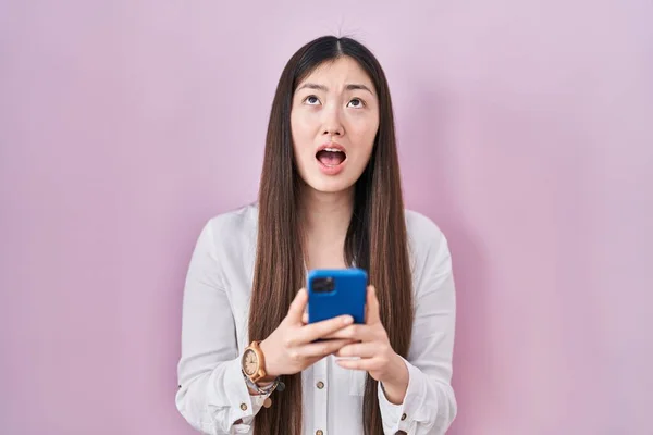 stock image Chinese young woman using smartphone typing message angry and mad screaming frustrated and furious, shouting with anger looking up. 