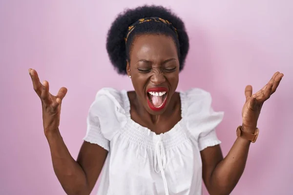 ピンクの背景に立っている巻き毛を持つアフリカの女性は 腕を上げて興奮して叫んで目を閉じて成功のために狂気と狂気を祝います 勝者のコンセプト — ストック写真