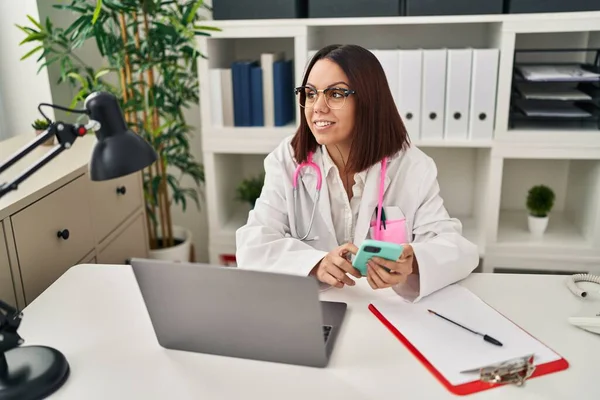 stock image Young beautiful hispanic woman doctor using smartphone working at clinic