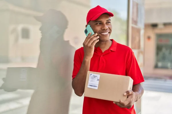 Young Latin Man Delivery Worker Holding Package Talking Smartphone Street — Stok fotoğraf