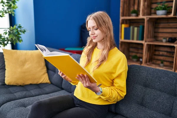 Young Blonde Woman Reading Book Sitting Sofa Home — Zdjęcie stockowe