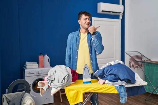 Młody Latynoski Mężczyzna Prasowanie Ubrania Domu Wskazując Kciuk Górę Boku — Zdjęcie stockowe