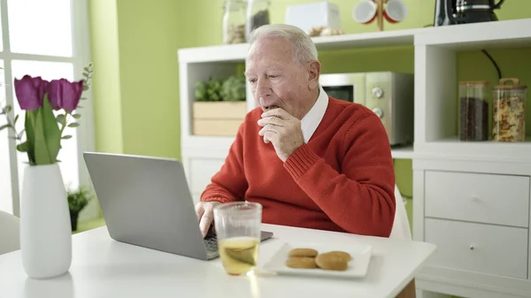 senior eating cookies and drinking juice using laptop at home
