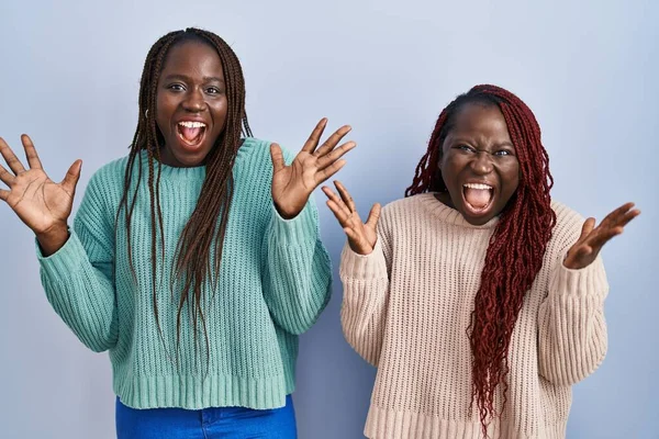 青い背景の上に立っている2人のアフリカ人女性は 狂気を祝い 興奮して叫んで腕を上げて開いた目で成功に驚いています 勝者のコンセプト — ストック写真
