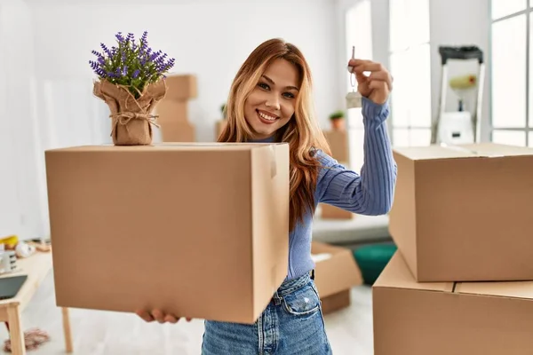 Young caucasian woman smiling confident holding package with lavender plant and key at new home