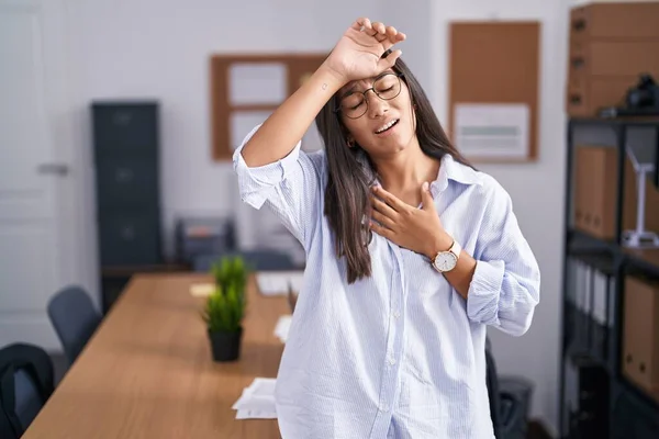 Young hispanic woman at the office touching forehead for illness and fever, flu and cold, virus sick