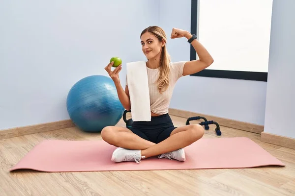 腕の筋肉を示す健康的なリンゴの強い人を保持スポーツウェアとタオルを身に着けている若いブロンドの女性 自信と力の誇り — ストック写真