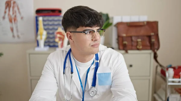 年轻的惊慌失措的医生坐在桌子上 表情严肃地坐在诊所里 — 图库照片
