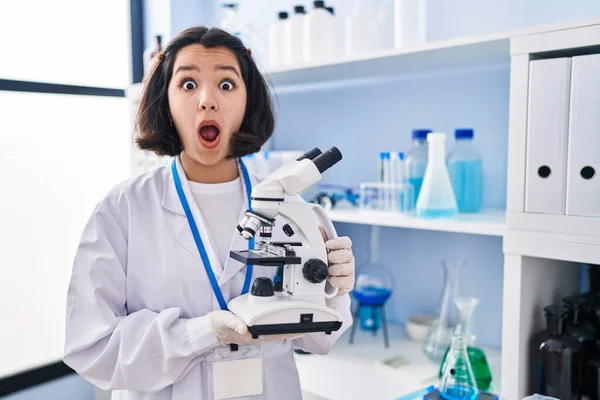 Młoda Latynoska Kobieta Pracująca Laboratorium Naukowca Trzymająca Mikroskop Przerażona Zszokowana — Zdjęcie stockowe