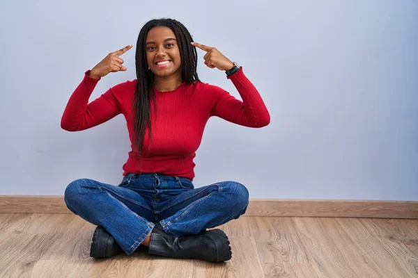 Joven Afroamericano Con Trenzas Sentado Suelo Casa Sonriendo Apuntando Cabeza —  Fotos de Stock