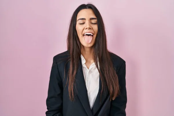 ピンクの背景にビジネススタイルを身に着けている若いブルネットの女性は面白い表情で幸せ舌を突き出す 感情の概念 — ストック写真