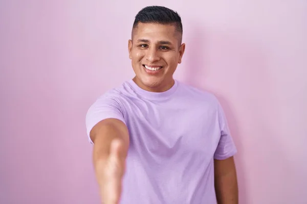 Молодой Латиноамериканец Стоящий Розовом Фоне Улыбаясь Дружелюбно Предлагая Рукопожатие Качестве — стоковое фото