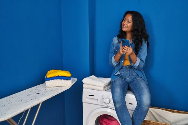 Young Chinese Woman Using Smartphone Waiting Washing Machine Laundry Room — Foto de Stock