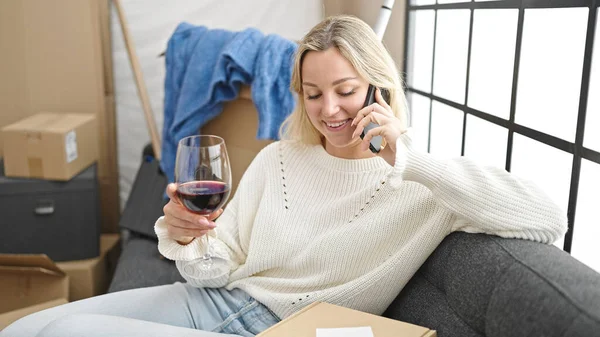 stock image Young blonde woman talking on the smartphone and drinking wine at new home