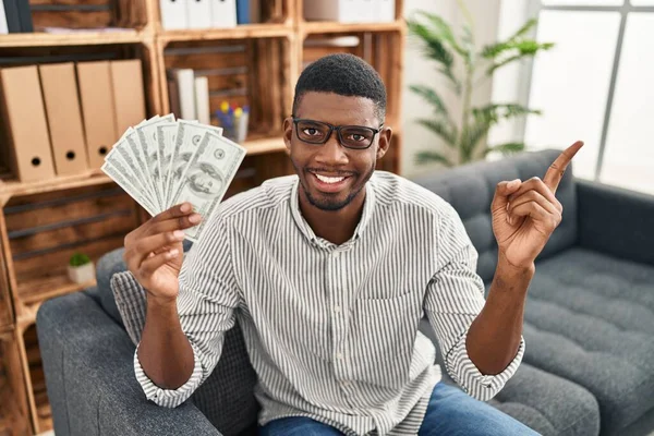 Africký Američan Drží Dolary Úsměvem Šťastný Ukazuje Rukou Prstem Stranu — Stock fotografie