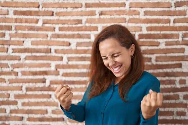 布鲁内特的女人站在砖墙上 非常高兴而兴奋地举起双臂做获胜者的手势 微笑着 尖叫着要成功 庆祝概念 — 图库照片