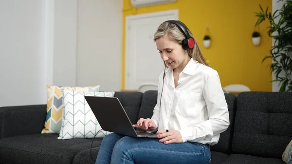 Młoda Blondynka Pomocą Laptopa Słuchawek Siedzi Kanapie Domu — Zdjęcie stockowe