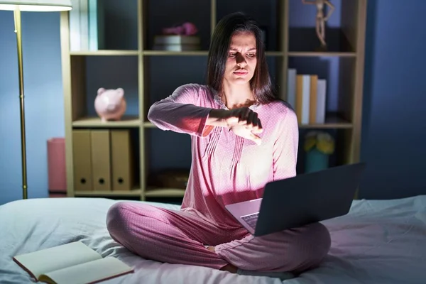 Young hispanic woman using computer laptop on the bed looking unhappy and angry showing rejection and negative with thumbs down gesture. bad expression.