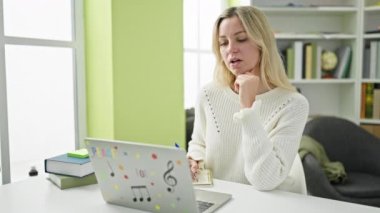 Kütüphanede dizüstü bilgisayar kullanan genç sarışın kız öğrenci.