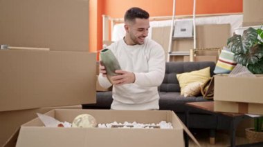 Young hispanic man unpacking cardboard box at new home