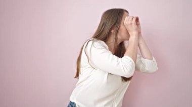 Genç, güzel, İspanyol bir kadın, pembe arka planda sürpriz bir ifadeyle dürbün hareketi yapıyor.