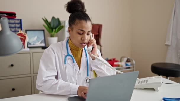 Νεαρή Αφροαμερικανίδα Γιατρός Που Χρησιμοποιεί Φορητό Υπολογιστή Μιλώντας Στο Τηλέφωνο — Αρχείο Βίντεο