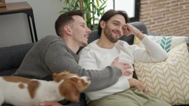 İki erkek birbirini kucaklıyor. Kanepede köpek gibi oturuyorlar.
