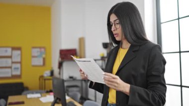 Young beautiful hispanic woman business worker reading document at office