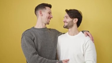 Birbirlerine sarılan iki erkek izole edilmiş sarı arka planda duruyor.