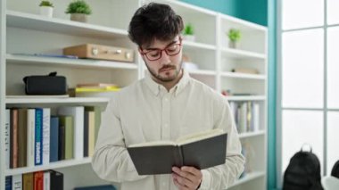 Genç İspanyol öğrenci kitap okuyor kütüphanede sessizlik jesti yapıyor.
