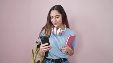 Genç, güzel İspanyol kız öğrenci izole edilmiş pembe arka plan üzerinde akıllı telefon rehberi kullanıyor.