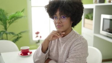 Genç Afro-Amerikan kadın evde masada kendinden emin bir şekilde oturuyor.