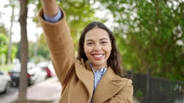 Genç, güzel, İspanyol bir kadın gülümsüyor. Parkta elleri ile çerçeve hareketi yapıyor.