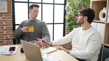 Not defterine yazan iki iş ortağı ofiste kahve içiyor.