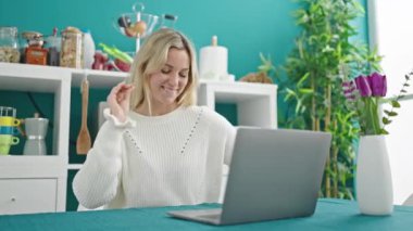 Genç sarışın kadın yemek odasında dizüstü bilgisayar dansı yapıyor.