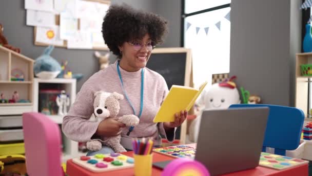 若いアフリカ系アメリカ人の女性の就学前の先生読書ストーリー本上のビデオコールで幼稚園 — ストック動画