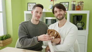 İki erkek, yemek salonunda masaya oturmuş kendinden emin bir şekilde gülümsüyor.