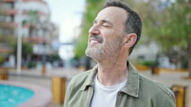 Orta yaşlı bir adam parkta kendinden emin bir şekilde gülümsüyor.