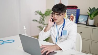 Genç İspanyol doktor laptopunu kullanıyor. Klinikte akıllı telefondan konuşuyor.