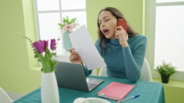 Genç, güzel, İspanyol bir kadın evde akıllı telefon okuyarak üzgün bir şekilde konuşuyor.