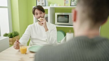 İki erkek, yemek salonunda kahvaltı ederken kendinden emin bir şekilde gülümsüyor.