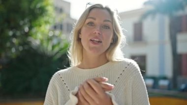 Young blonde woman smiling confident speaking at park