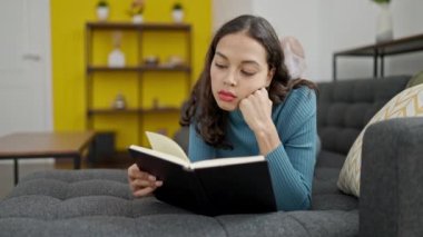 Evdeki kanepede uzanmış kitap okuyan güzel İspanyol kadın.